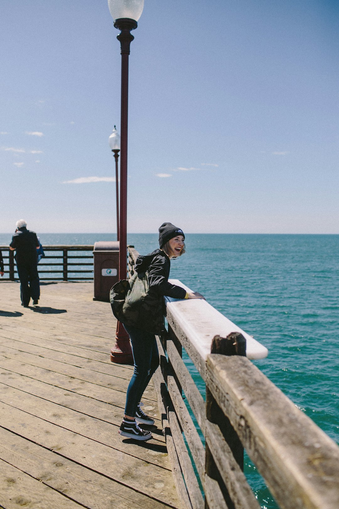 smiling woman standing near the fence beside the ocean