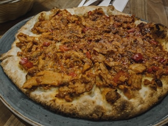 A pizza topped with generous portions of cooked chicken and red peppers, served on a stoneware plate. The base is crispy and slightly charred, with visible pieces of succulent meat and vegetables spread evenly.