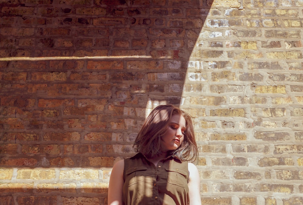 woman looking downwards beside brick wall