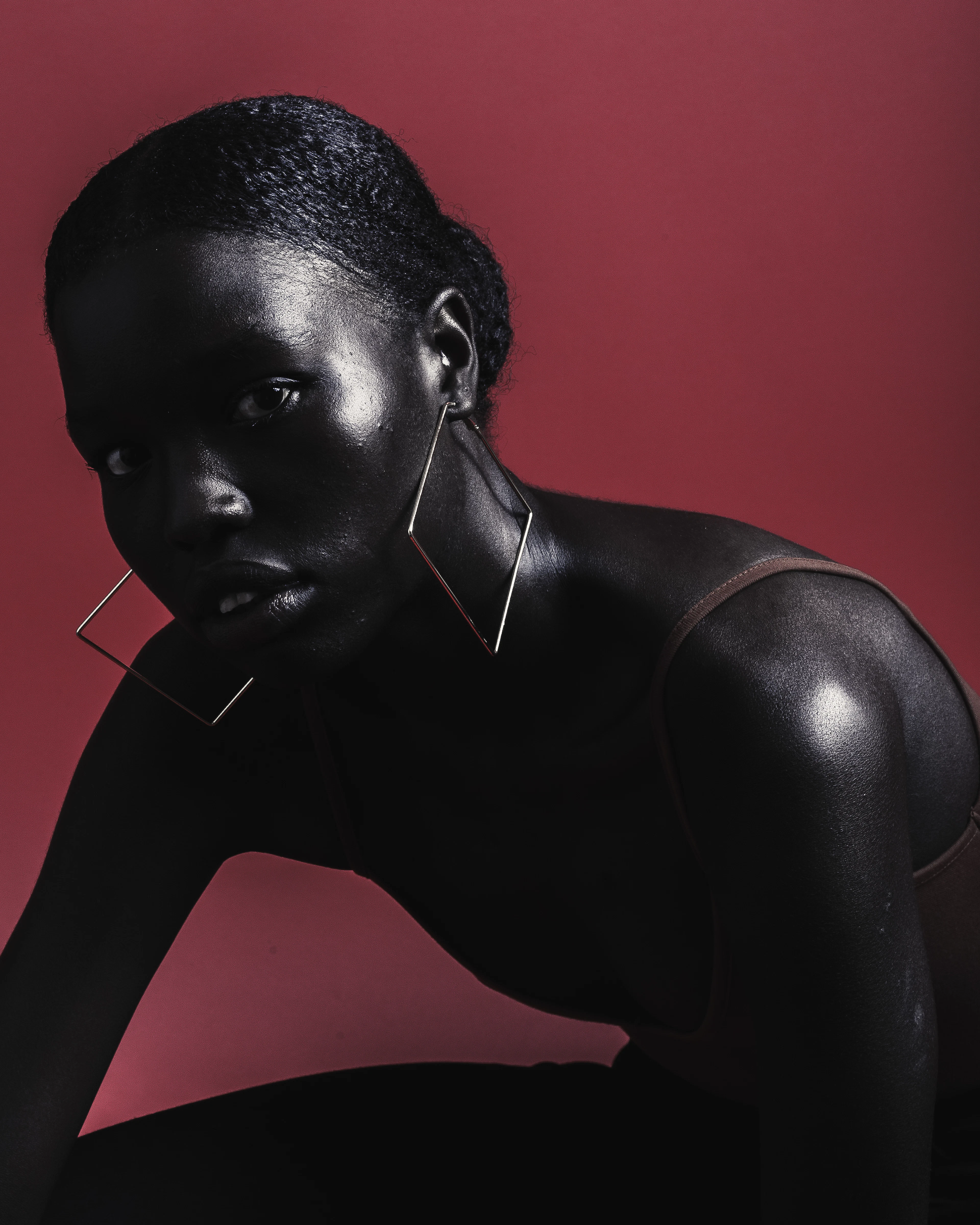 Editorial portrait with sculpted skin against deep burgundy