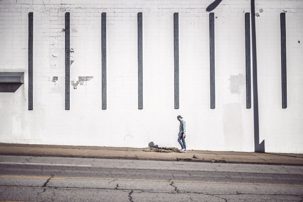 man walking at the side of the road beside wall