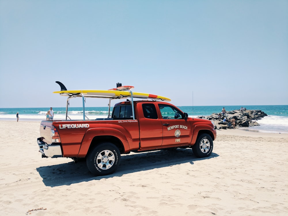 red lifeguard pickup truck with surfboard on roof parked on shore