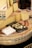 A selection of cheese is displayed, featuring several large wedges and slices of Comté cheese. Small cubes of cheese are arranged on a black slate board for sampling. The cheese wheels have distinctive labels with the Comté branding visible. A paper-wrapped block of cheese with a price written on it is also present.