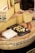 A selection of cheese is displayed, featuring several large wedges and slices of Comté cheese. Small cubes of cheese are arranged on a black slate board for sampling. The cheese wheels have distinctive labels with the Comté branding visible. A paper-wrapped block of cheese with a price written on it is also present.