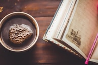 A notebook and pen beside a cup of coffee on a wooden desk.