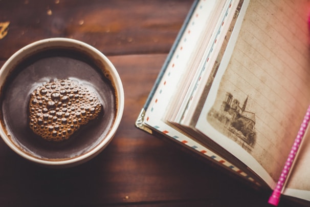 Close-up of a rustic wooden table with a steaming cup of coffee and an open journal