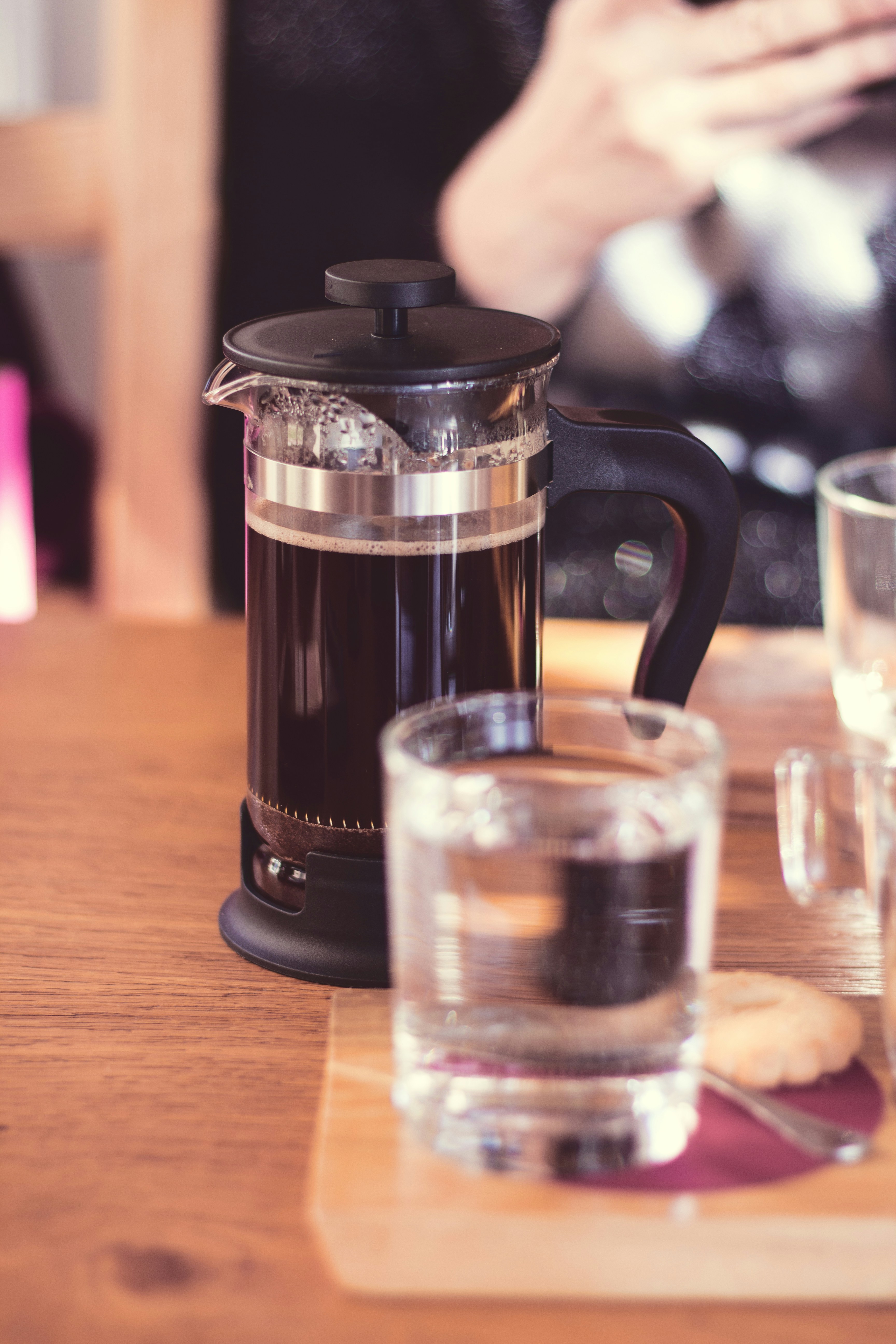 French press coffee maker with dark brew inside, plunger mid-press, wooden table, warm natural light