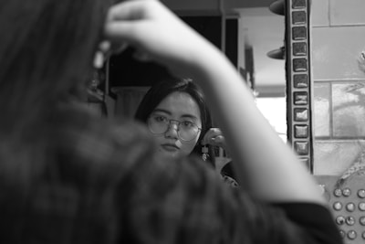 Close-up of a woman trying on elegant glasses in front of a mirror.