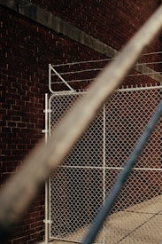 A chain-link fence stands against a brick wall, creating a robust and industrial setting. The angle of the photo includes metal bars in the foreground, which are blurred and cross diagonally, adding depth to the composition.