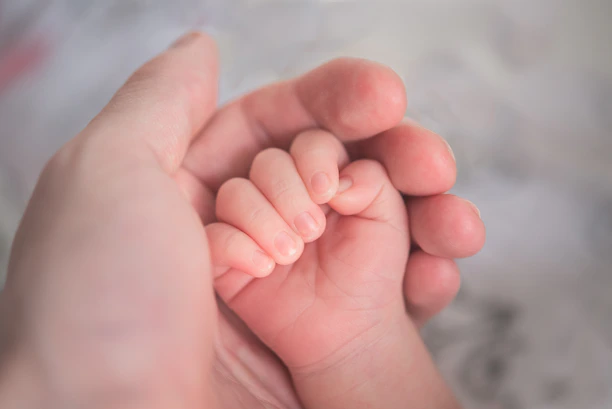 A tender moment of a father gently holding his daughter's hand in soft natural light.