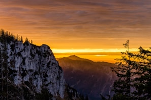 A hyper-realistic sunset over a rugged mountain ridge dusted with pine trees.