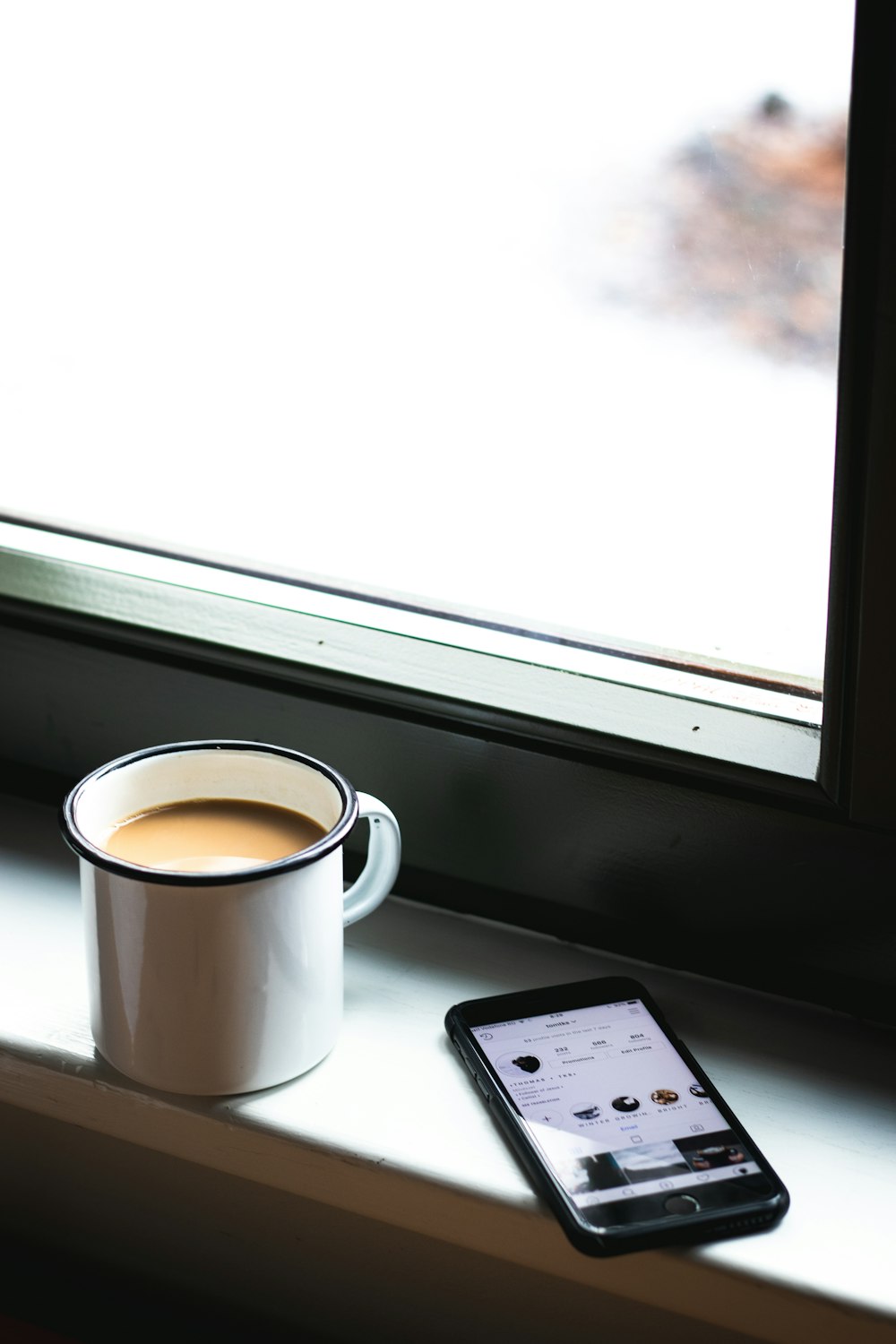 shallow focus photo of white ceramic mug beside space gray iPhone 6