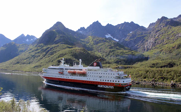Coastal ship sailing below steep snow-streaked mountains in Raftsundet, northern Norway