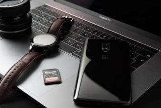black smartphone beside round silver watch on MacBook Pro