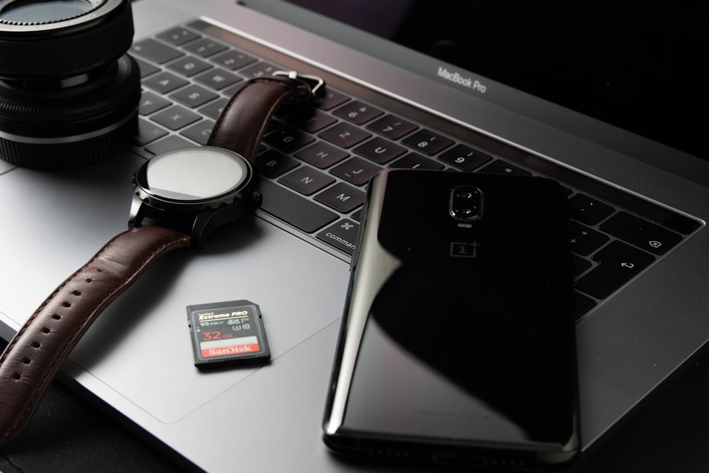 black smartphone beside round silver watch on MacBook Pro