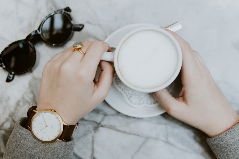 persona sosteniendo una taza de té blanca llena