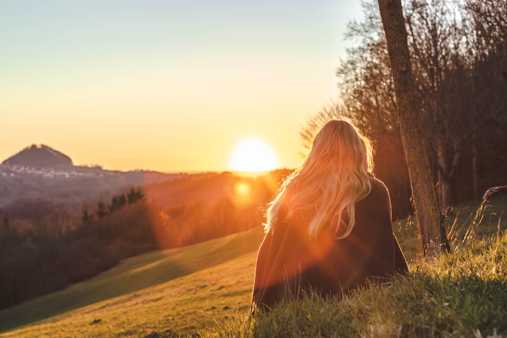 femme assise sur l’herbe verte regardant le soleil