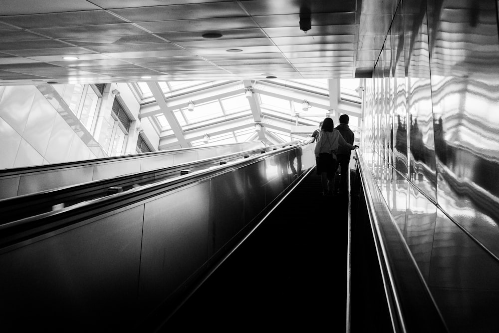 grayscale photo of man and woman riding on escalator