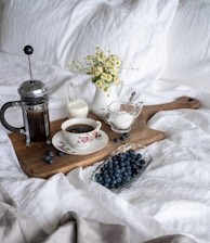 cup of coffee in between of coffee press and glass of sugar and milk on brown tray