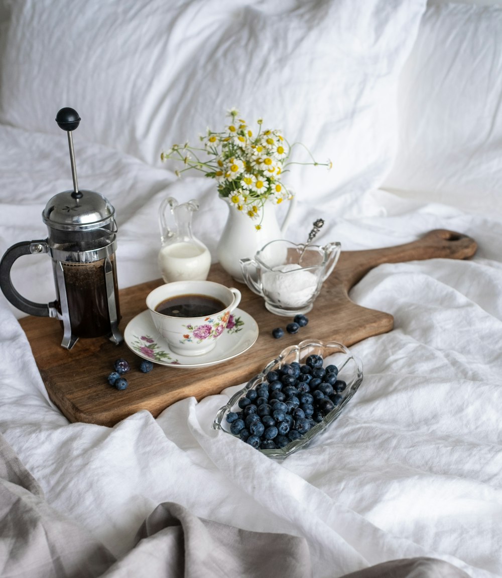 cup of coffee in between of coffee press and glass of sugar and milk on brown tray