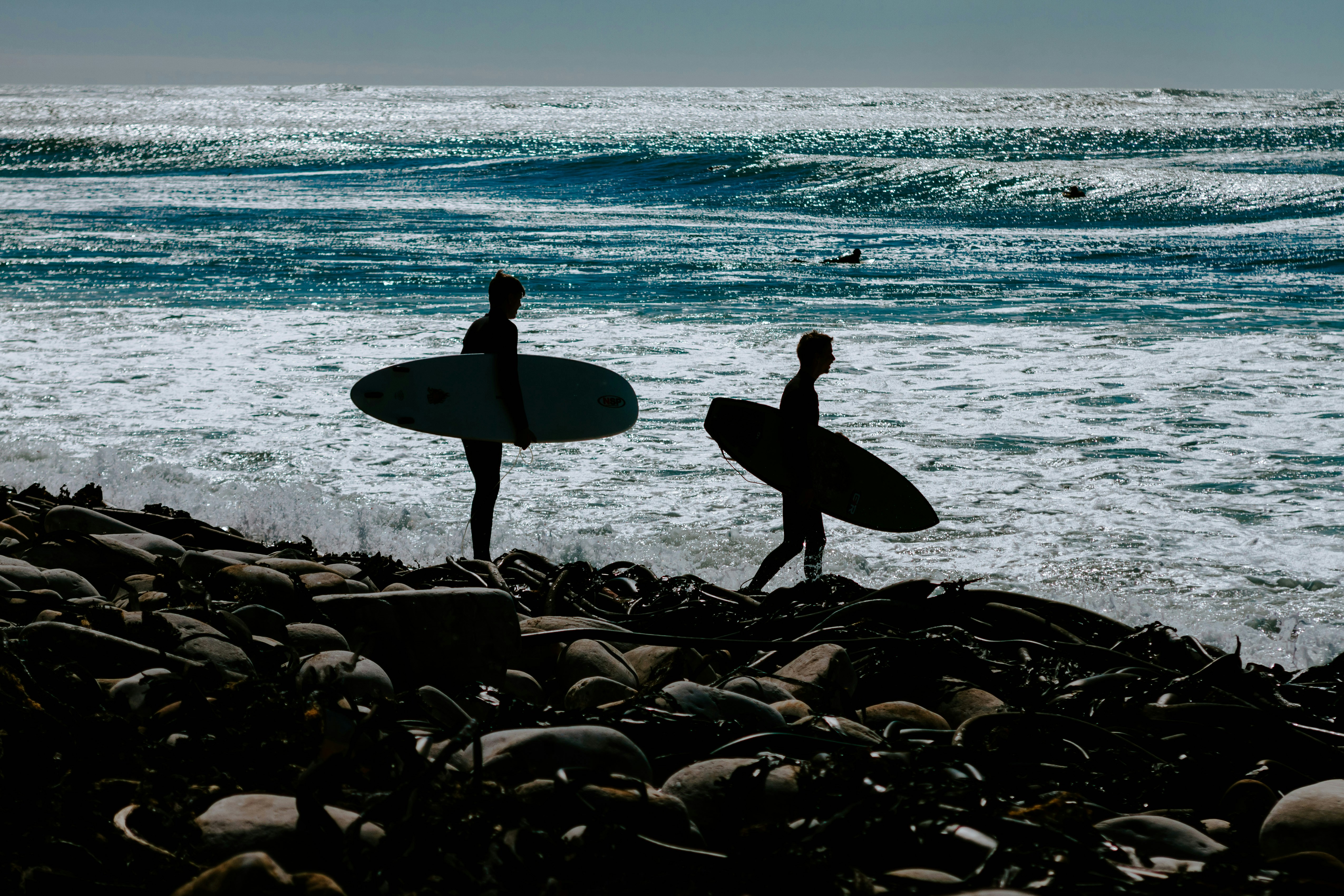 two persons holding surfboards near body of water careful teams background