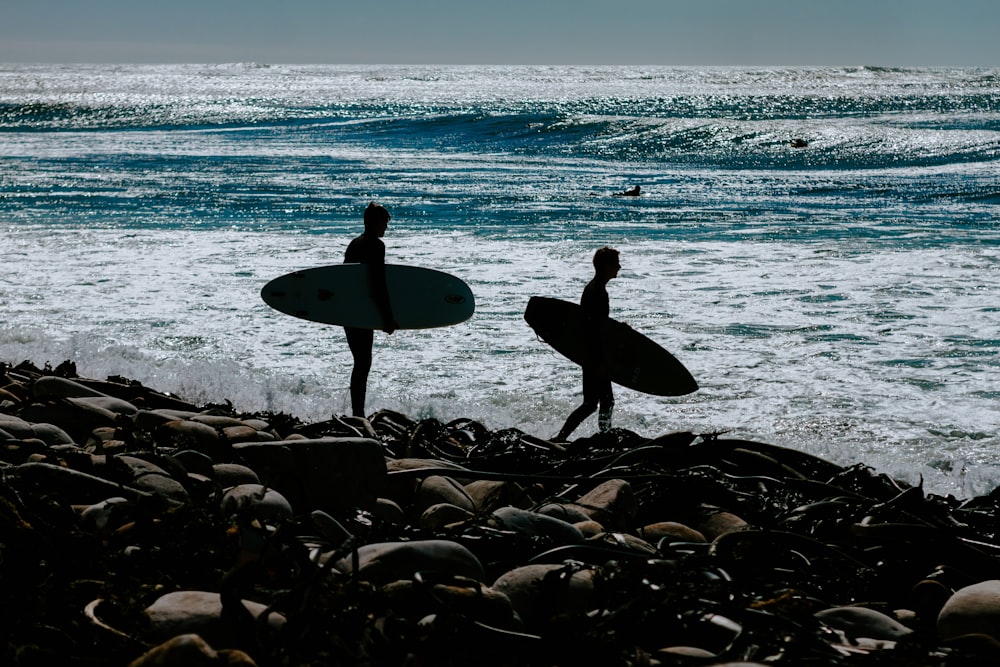 two persons holding surfboards near body of water