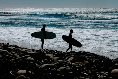 two persons holding surfboards near body of water careful google meet background