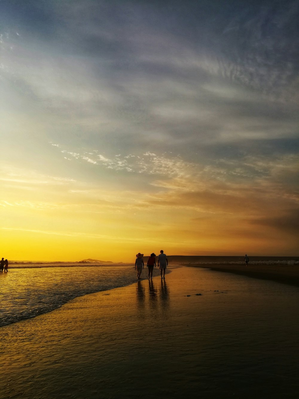 three person walking on shoreline during golden hour