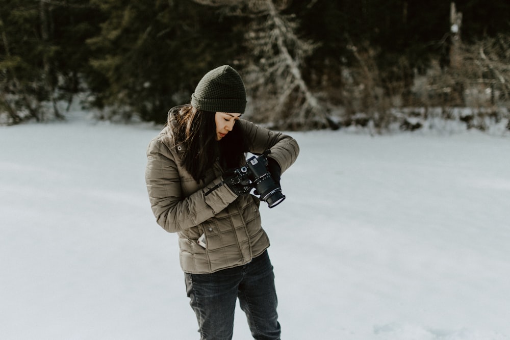 mujer sosteniendo una cámara digital negra de pie en el suelo lleno de nieve