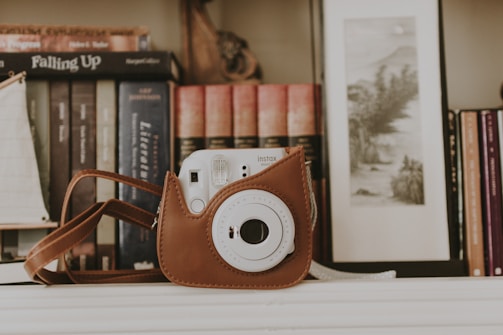 A monochrome photo of a vintage camera resting on a wooden desk beside a sketchbook filled with minimalist designs.