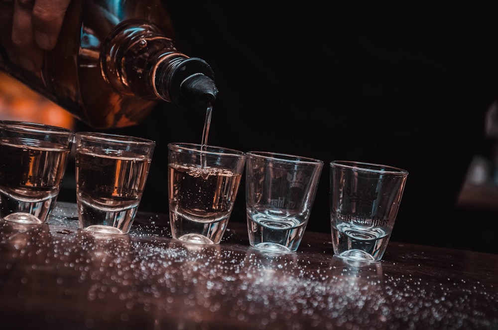 person pouring beverage on five shot glasses