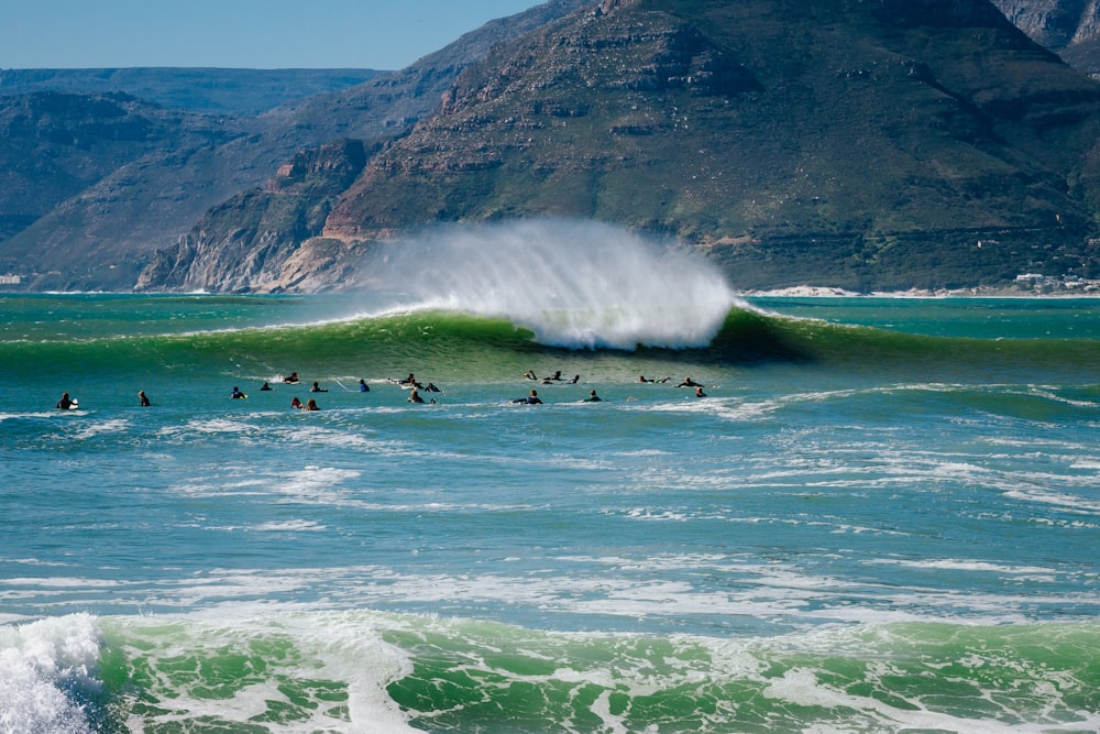 people on ocean with huge wave during daytime