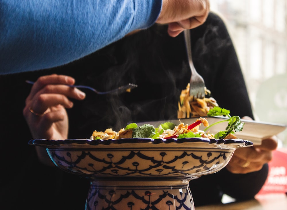 Fotografía de enfoque selectivo de una persona sosteniendo un tenedor recogiendo alimentos cocidos