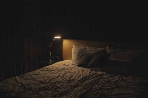 A quiet bedroom at night with soft shadows and a glowing bedside lamp, perfect for unwinding.
