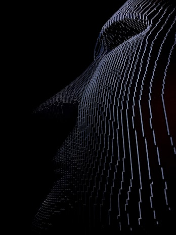 A textured surface with a wave-like pattern is depicted, consisting of numerous vertical lines or elements that gently curve and undulate across a dark, shadowy background. The intricate structure creates a sense of depth and movement.