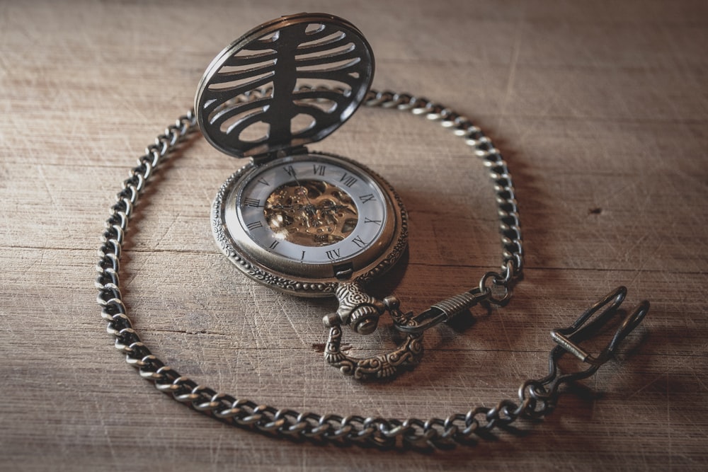 round silver-colored pocket watch on table