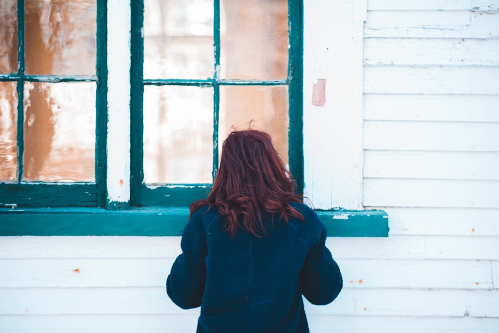 Mujer con abrigo azul de pie cerca de la ventana