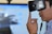 A person is wearing a virtual reality headset, touching the side of the device with their hand as if adjusting it. The background appears blurry, suggesting focus on the individual and the VR device.