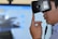 A person is wearing a virtual reality headset, touching the side of the device with their hand as if adjusting it. The background appears blurry, suggesting focus on the individual and the VR device.