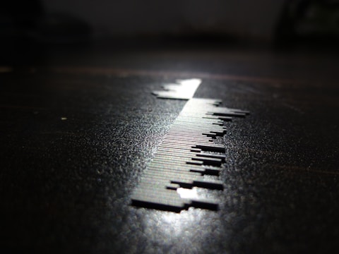 A close-up of a series of small, thin, vertical metal pieces resembling a barcode is depicted on a surface. The lighting creates a sharp shadow, enhancing the contrast between the metallic elements and the dark background.
