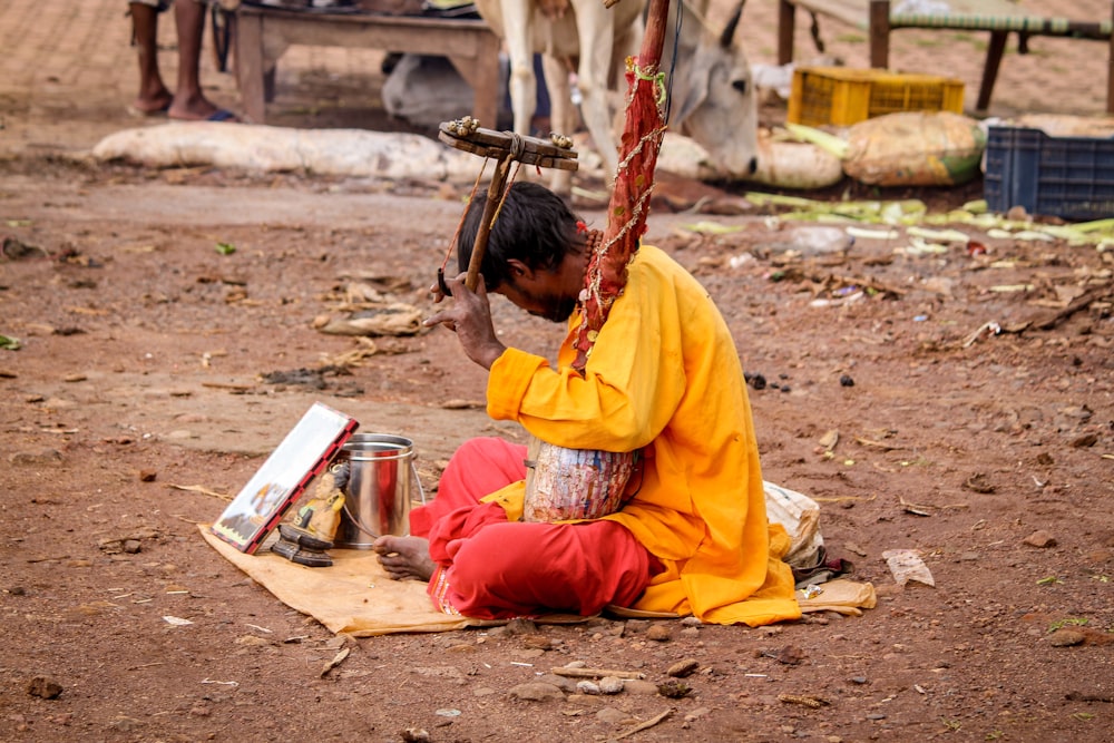 a man sitting on the ground next to a cow