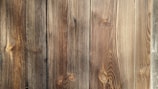 Four wooden planks with visible grain patterns and knots, characterized by a natural brown color and varied texture.