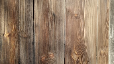 Four wooden planks with visible grain patterns and knots, characterized by a natural brown color and varied texture.