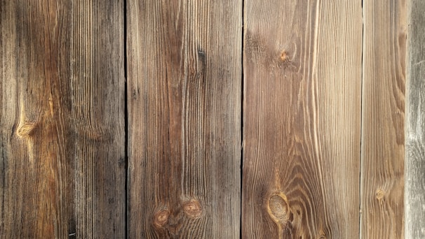 Four wooden planks with visible grain patterns and knots, characterized by a natural brown color and varied texture.