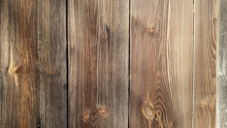 Four wooden planks with visible grain patterns and knots, characterized by a natural brown color and varied texture.