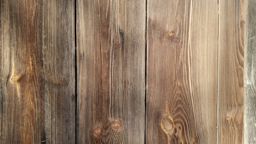 Four wooden planks with visible grain patterns and knots, characterized by a natural brown color and varied texture.