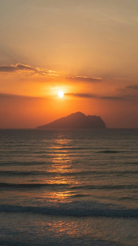 從宜蘭頭城海岸望向龜山島，太陽在龜山島上方，海面映著橘色光線
