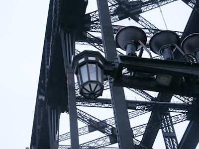 A close-up view of a large, intricate metal structure featuring a black and white lantern and two horn-shaped objects. The metalwork displays a complex pattern of intersecting beams and latticework.