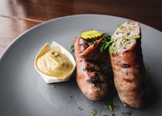 two sausages on a plate with mustard on the side