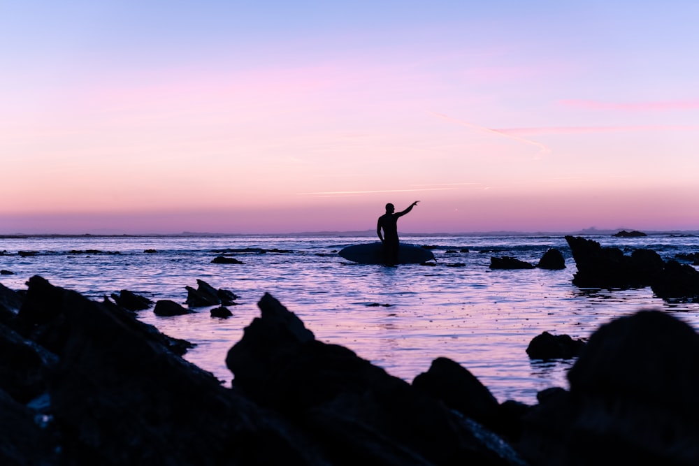 silhouette of person standing on rock beside beach